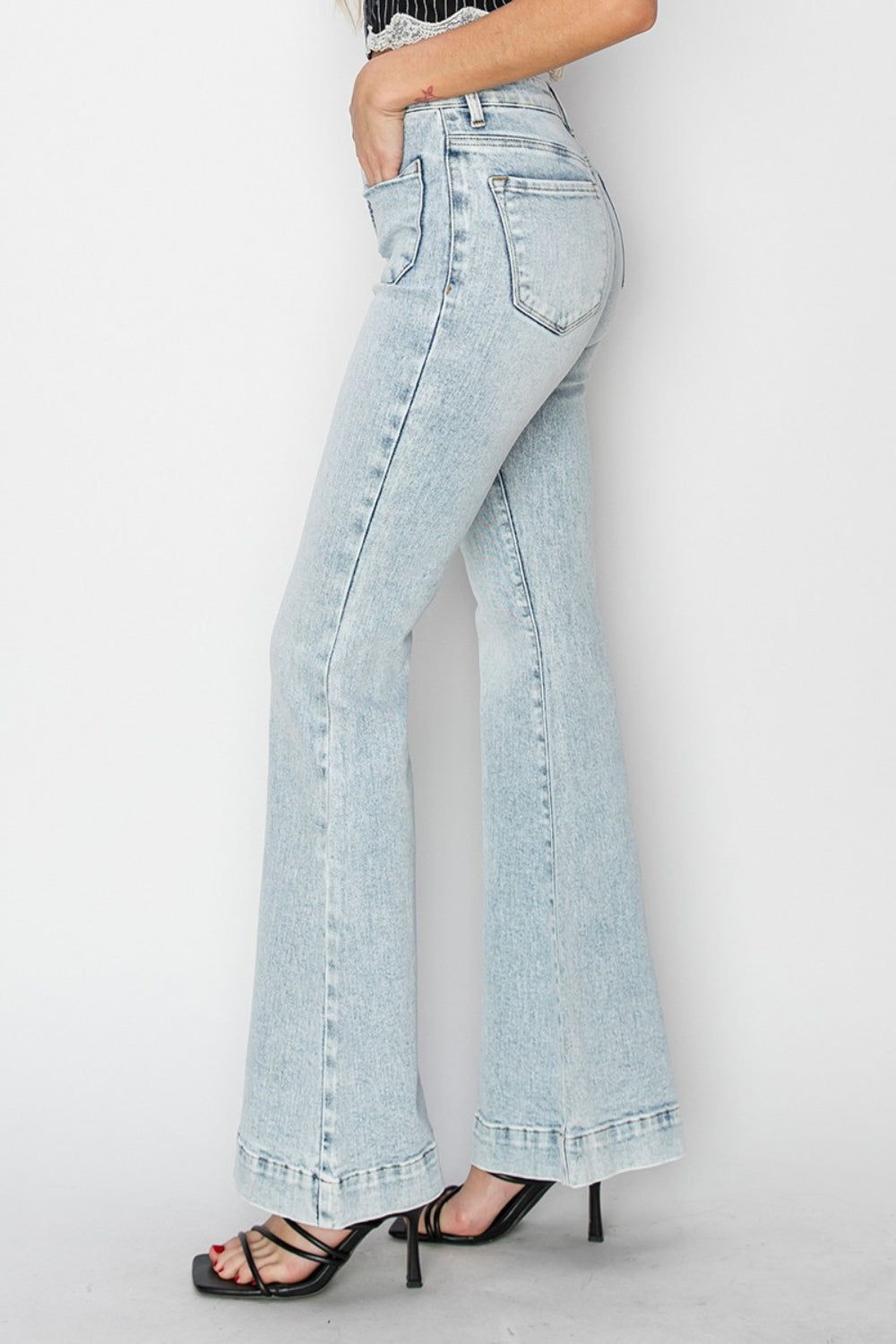 A person wearing Risen Full Size High Rise Front Patch Pocket Flare Jeans in a light wash, paired with black strappy sandals, stands against a white background.