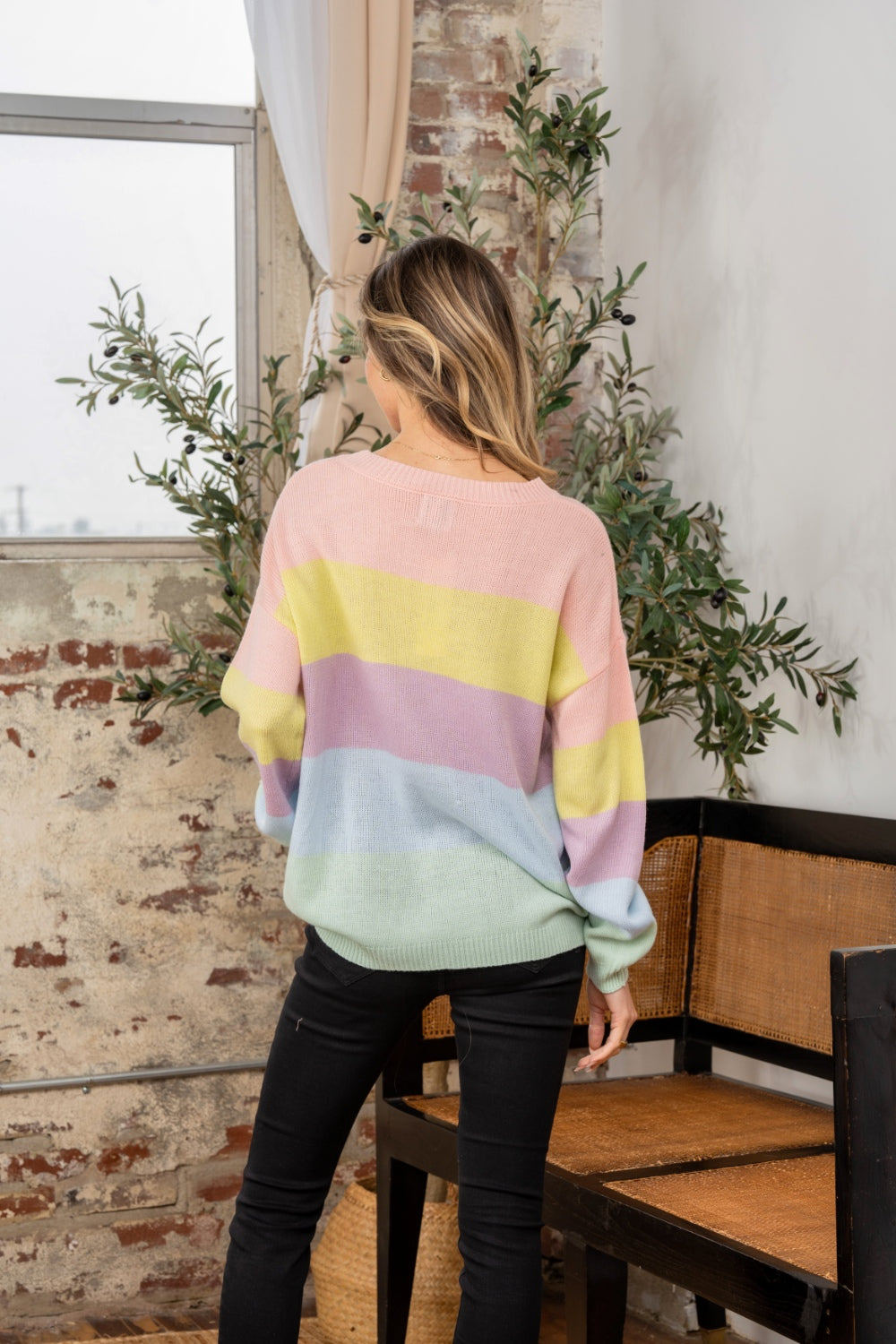 A woman wearing the Sew In Love Full Size Color Block Round Neck Dropped Shoulder Sweater stands indoors next to a chair and potted plant.