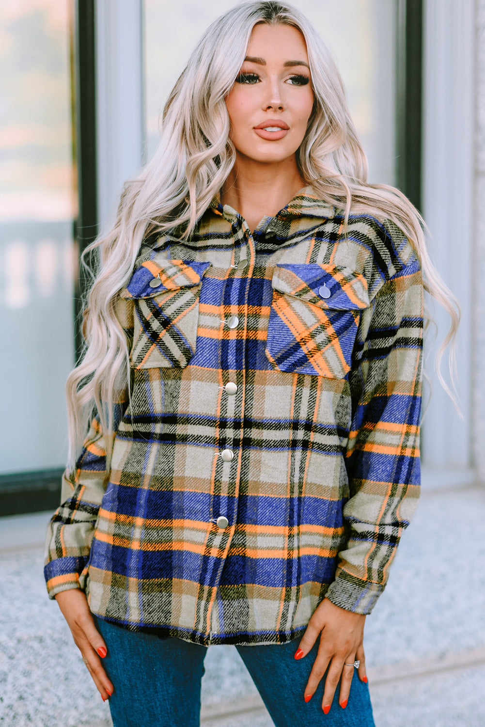 A person wearing a Brown Plaid Button Up Long Sleeve Flannel Shacket layered over a white top with ripped jeans and holding a brown handbag stands against a textured gray wall.