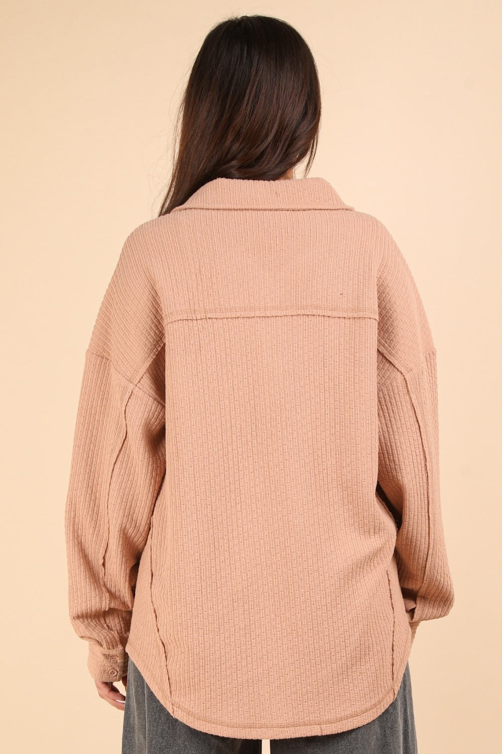 A woman wearing the VERY J Button Down Textured Knit Shacket in an oversized beige style over a black top stands against a plain background, showcasing the perfect transitional piece for any wardrobe.