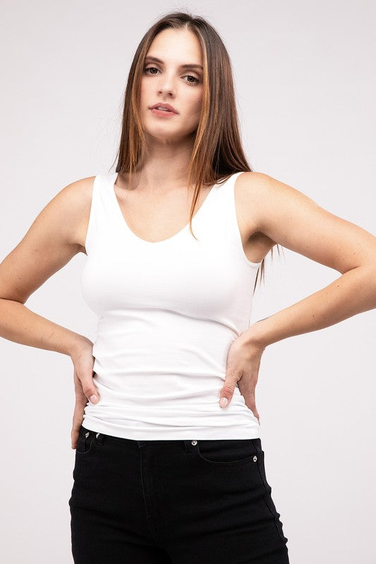 A woman in a white Front & Back 2-Way V-Neck Seamless Tank and black pants, standing with hands on hips and looking at the camera.