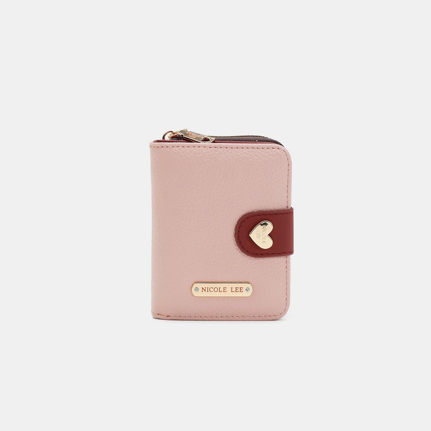 The Nicole Lee USA Solid Heart Bifold Wallet is a small, pink, vegan leather accessory that features a red strap and gold hardware. It includes a zipper and is adorned with a heart-shaped embellishment. The name "Nicole Lee" is prominently displayed on the front.