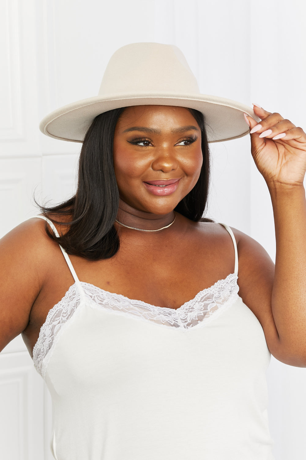 A woman with shoulder-length hair, wearing a Fame Ride Along Fedora Hat in beige with a black band, is seen from behind against a white background.