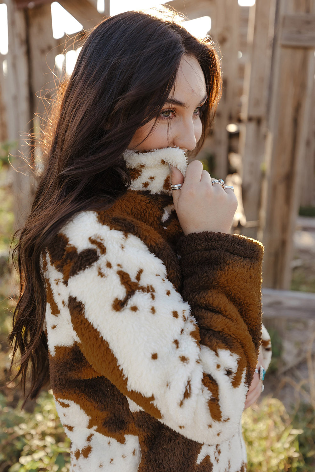 A person wearing a Zip Collar Cow Print Fleece Sweatshirt and light blue jeans stands outdoors with their back to the camera, showcasing the skin-friendly fleece material.