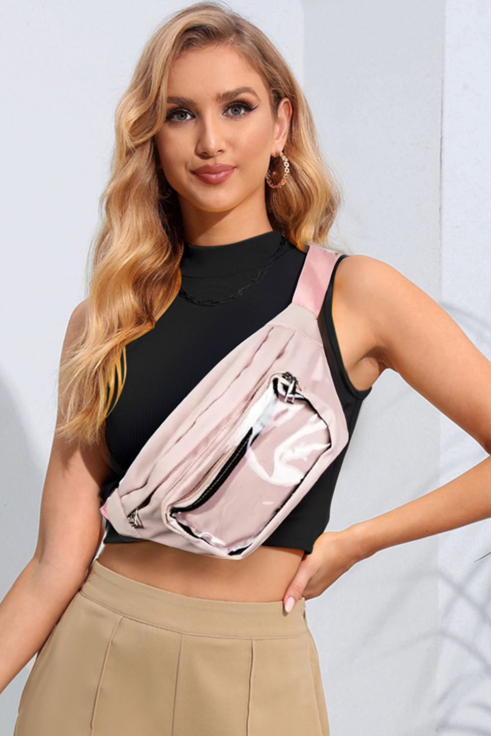 A woman wearing a black sleeveless top and beige pants showcases the Fame Adjustable Strap Sling Bag, styled as a pink crossbody fanny pack, against a light background. Her long, wavy blonde hair complements the look of this versatile accessory, ideal for everyday use.