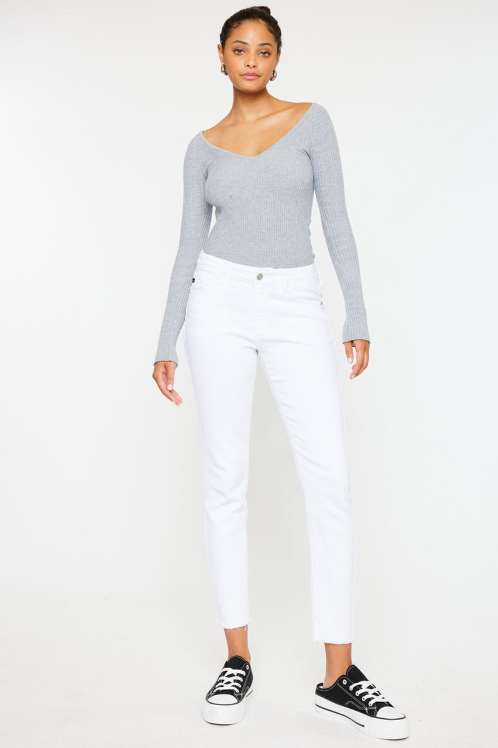 A person models a versatile gray long-sleeve top paired with flattering fit Kancan Mid Rise Ankle Skinny Jeans and sleek black sneakers, all set against a pristine white background.