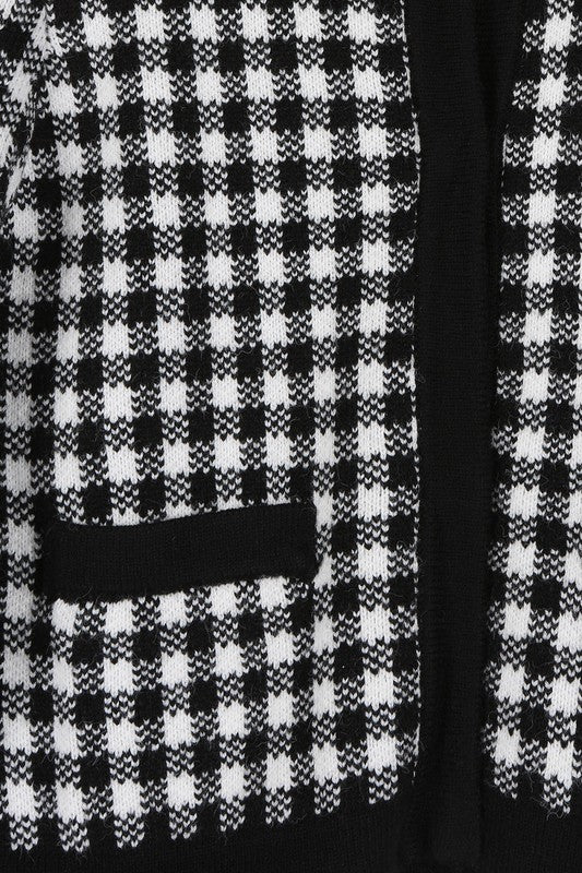 A woman dressed in the Black Check Knitted Jacket, featuring snap buttons and functional pockets, complemented by black pants, stands against a white background.