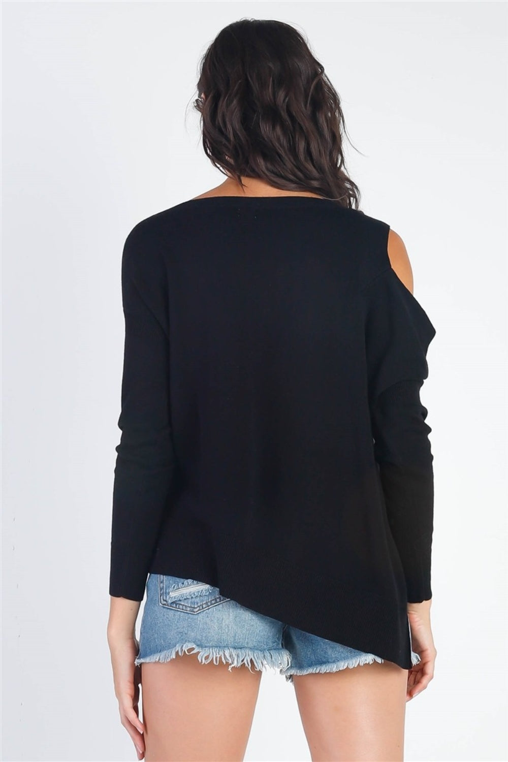 A person wearing the UNIQ Cold Shoulder Long Sleeve Knit Top in black and distressed denim shorts stands against a plain white background, effortlessly showcasing a versatile wardrobe choice.