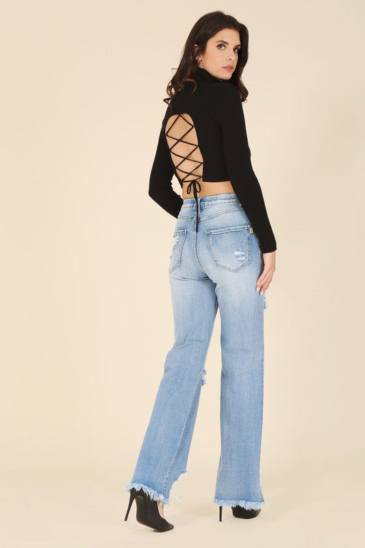 A woman wearing a stylish black mock neck lace-up open back top, paired with light blue ripped jeans.