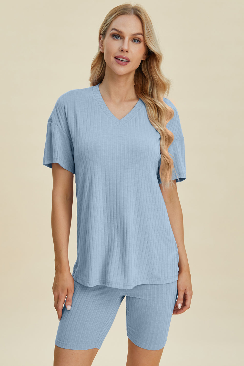 A woman with long blonde hair wearing the Basic Bae Full Size Ribbed V-Neck Short Sleeve Top and Shorts Set in rust stands against a plain background. This stylish two-piece set is made from a comfortable, stretchy fabric that is also machine washable.