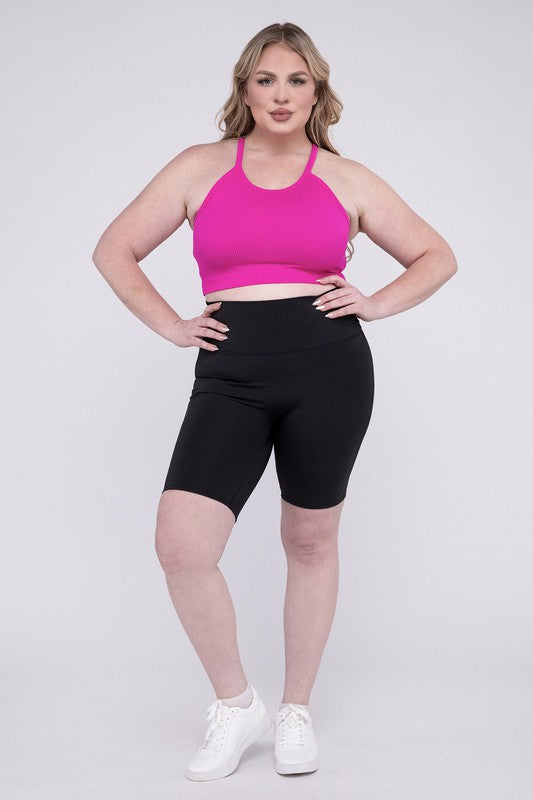 Against a plain background, a person showcases the Plus Athletic High Rise Biker Shorts in coral, crafted from high-quality athletic fabric and paired with a pink top.