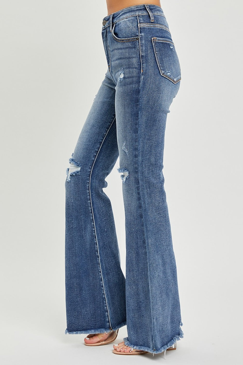 A person is wearing RISEN High Waist Distressed Fare Jeans, characterized by a high-waisted fit with minor rips and frayed hems, standing against a neutral background.