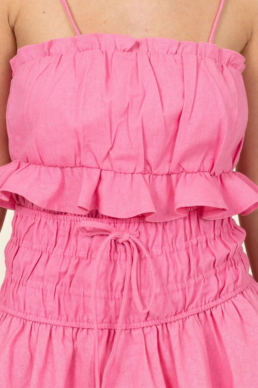 A person wearing a pink cami crop top and skort set with adjustable spaghetti straps stands against a neutral background.