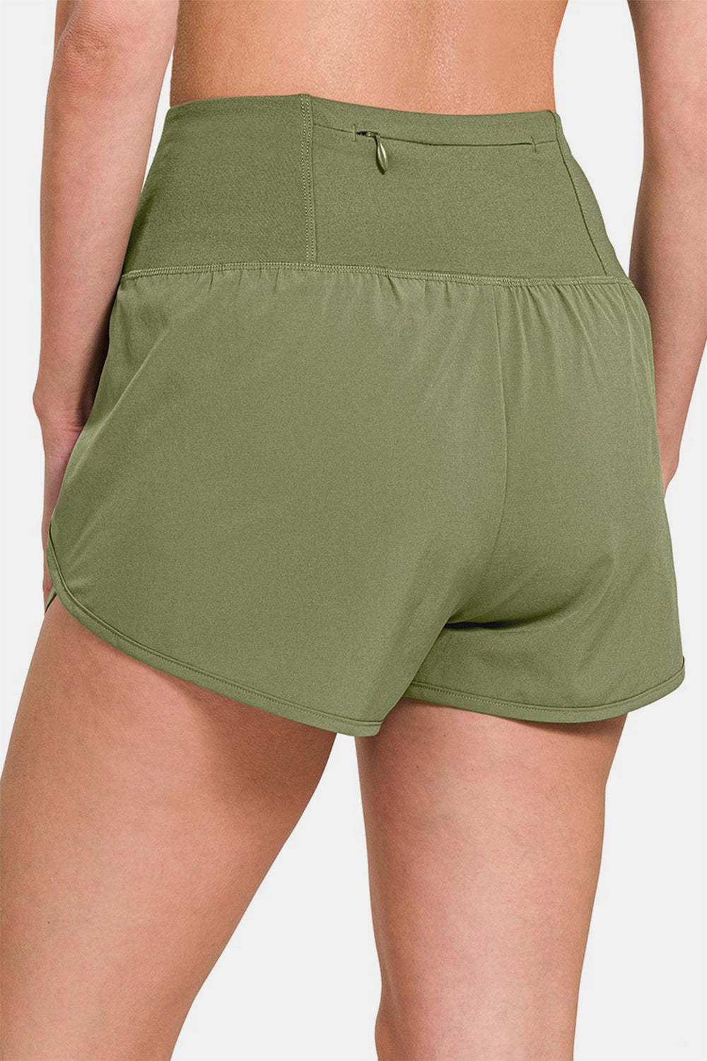 Individual sporting Zenana High-Waisted Zippered Back Pocket Active Shorts in light green, featuring a wide waistband, side slits, and a convenient zippered back pocket—ideal for active wear.