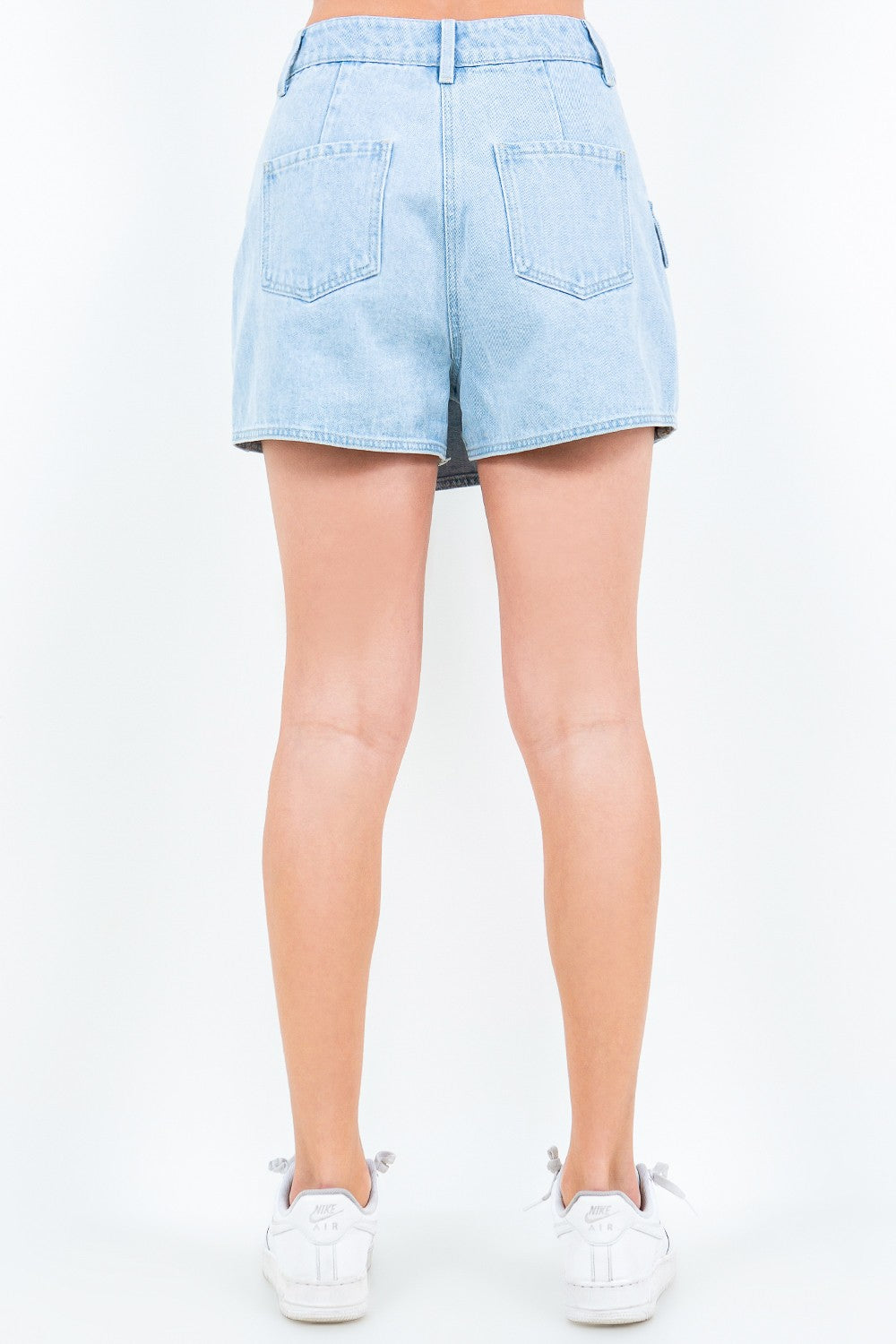 A person wears the American Bazi Cargo Pocket Mini Skort in light blue denim, featuring a large front pocket and button waist closure, paired with white sneakers.