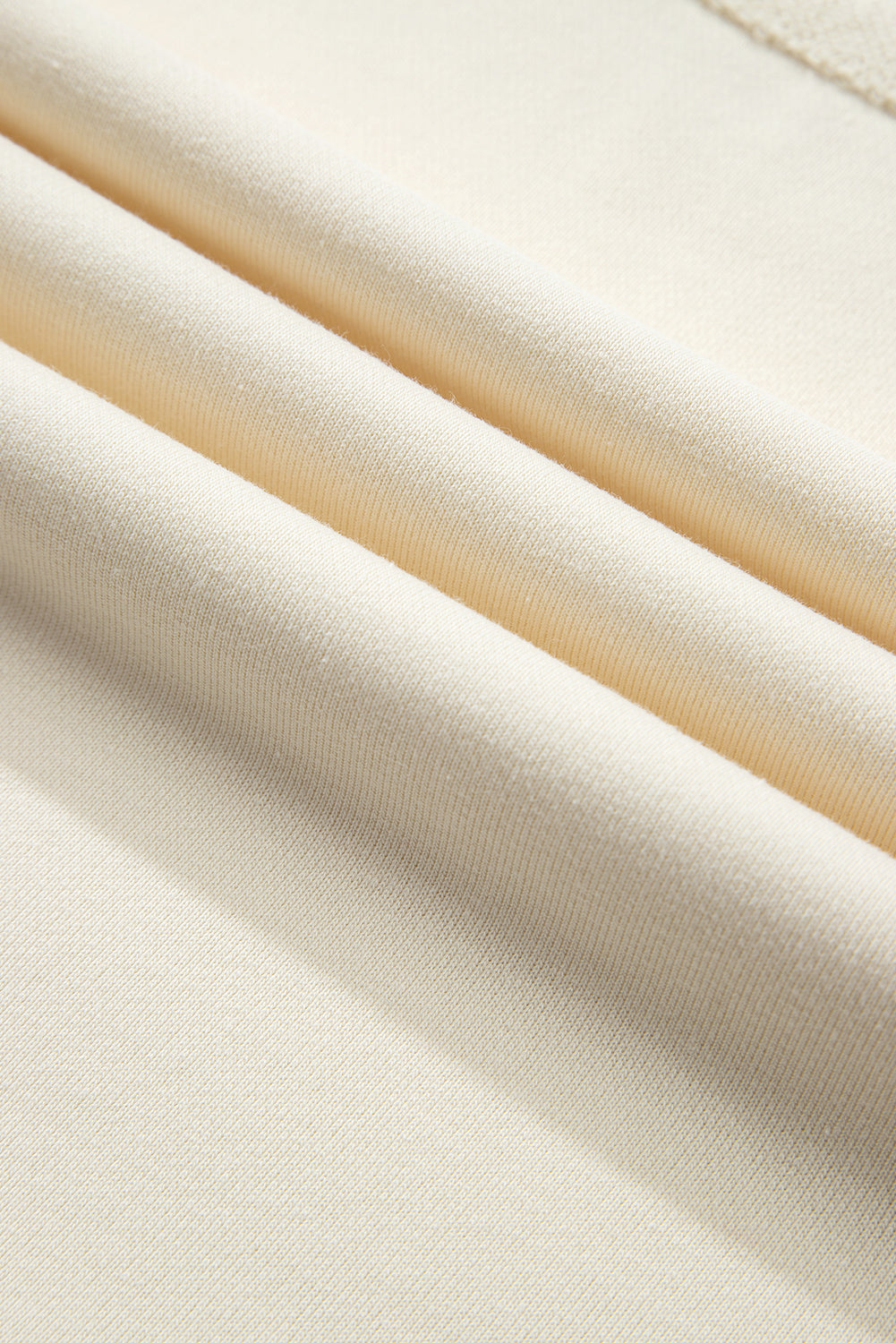 A person with long, wavy, light brown hair stands facing away, wearing the Beige Star Patchwork Exposed Seam Oversized Sweatshirt paired with denim shorts. The background is a plain, light peach wall, adding an edgy vibe to the look.