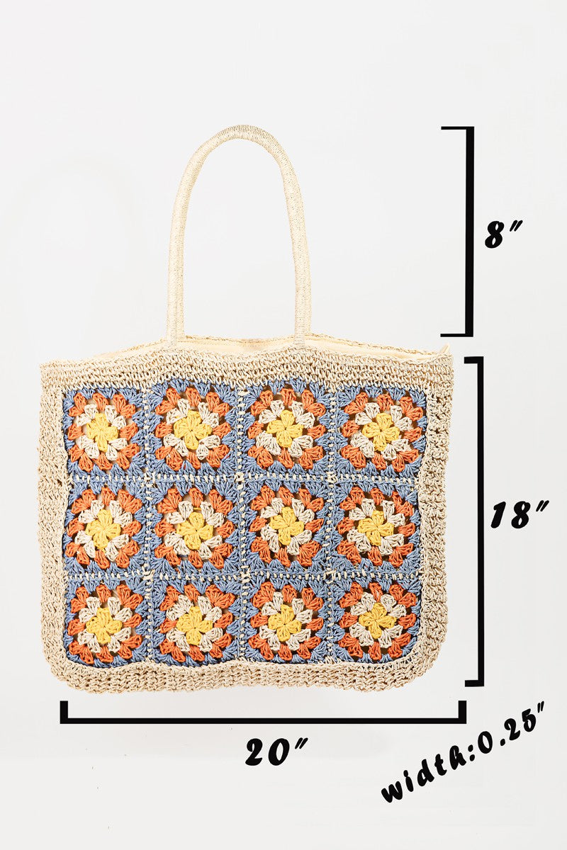 The Fame Flower Braided Tote Bag is a crocheted accessory with bohemian flair, featuring a grid of colorful flower patterns on the front. It showcases squares in orange, yellow, and blue on a natural fiber background.