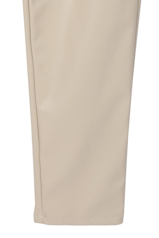 A person wearing a white sweater and black Vegan leather pants with hands in the pockets.