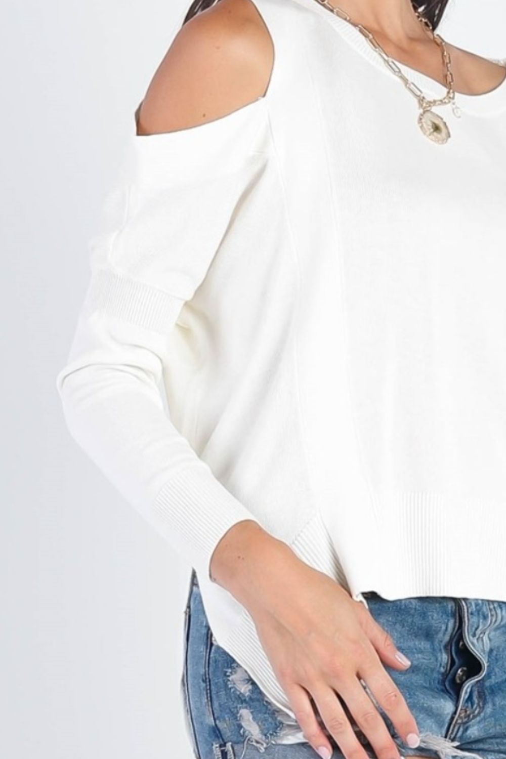 A person wearing the UNIQ Cold Shoulder Long Sleeve Knit Top in black and distressed denim shorts stands against a plain white background, effortlessly showcasing a versatile wardrobe choice.