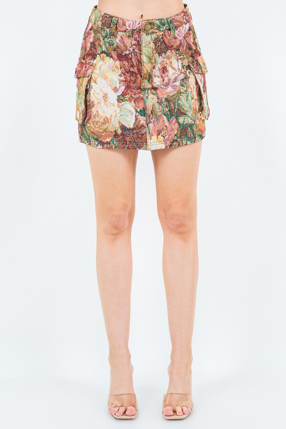 A person wearing a mini-length American Bazi Jacquard Weave Cargo Pocket Skirt with a delightful floral pattern and clear, open-toed heels stands against a plain background.