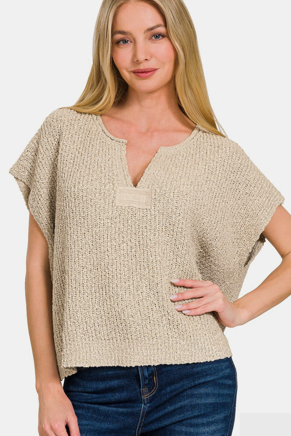 A person with long blonde hair is wearing a Zenana Short Sleeve Side Slit Sweater in a textured beige design, paired with denim jeans, and posing against a plain background.