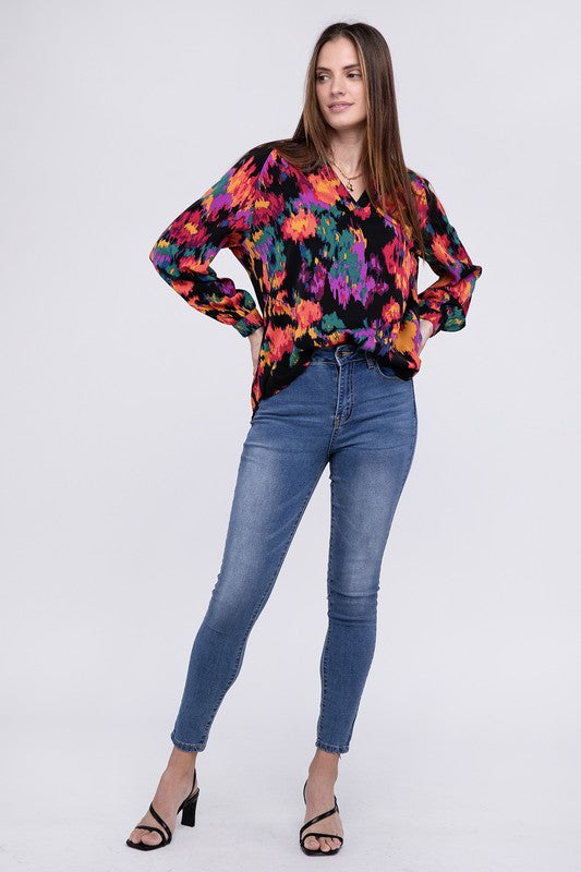 A person dressed in a vibrant Floral Raglan Sleeve Blouse featuring a V-neck stands against a plain backdrop, paired with jeans.