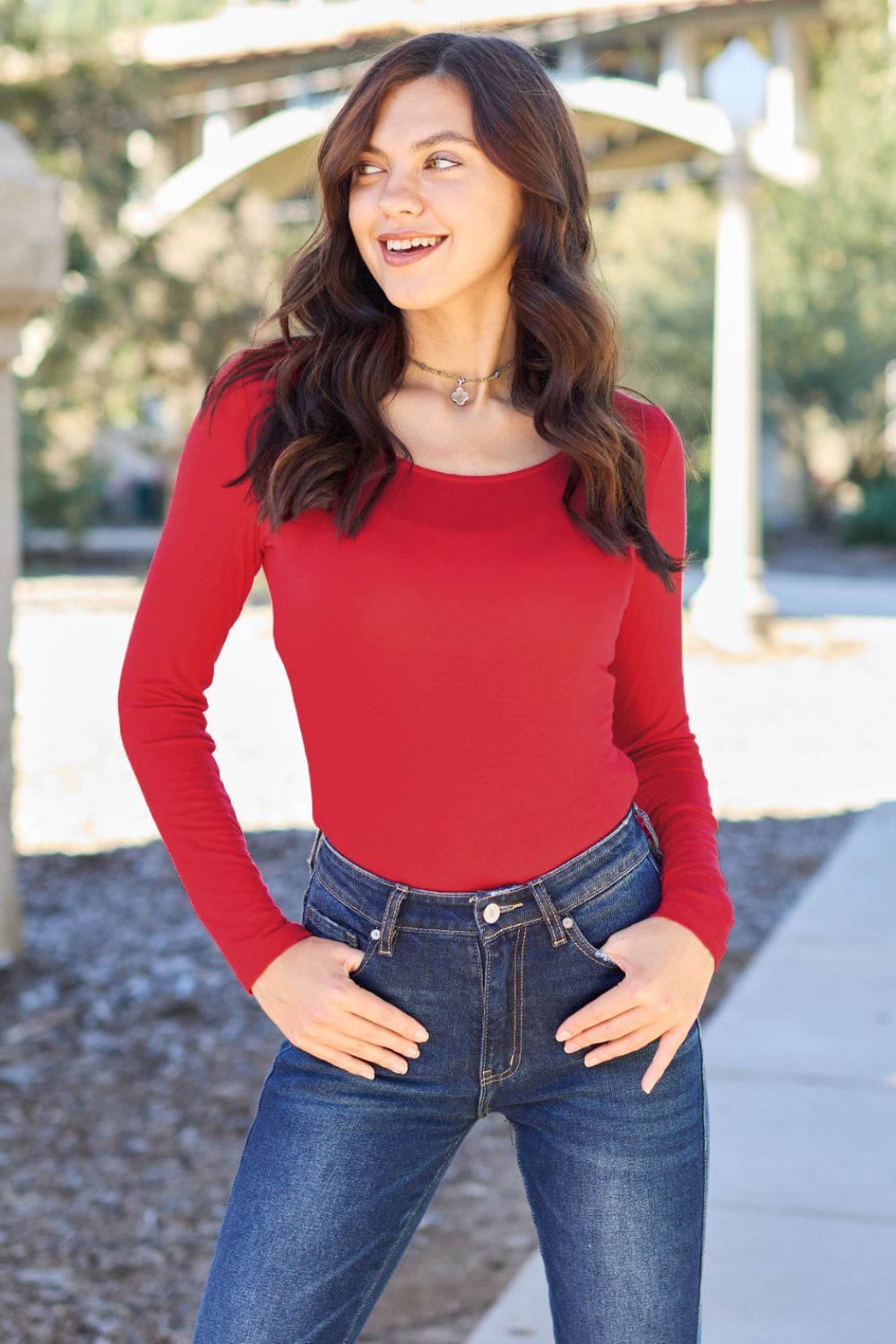 A person poses confidently in the Basic Bae Full Size Round Neck Long Sleeve Bodysuit, made from a rayon spandex blend, with one hand touching their neck and the other resting on their hip.