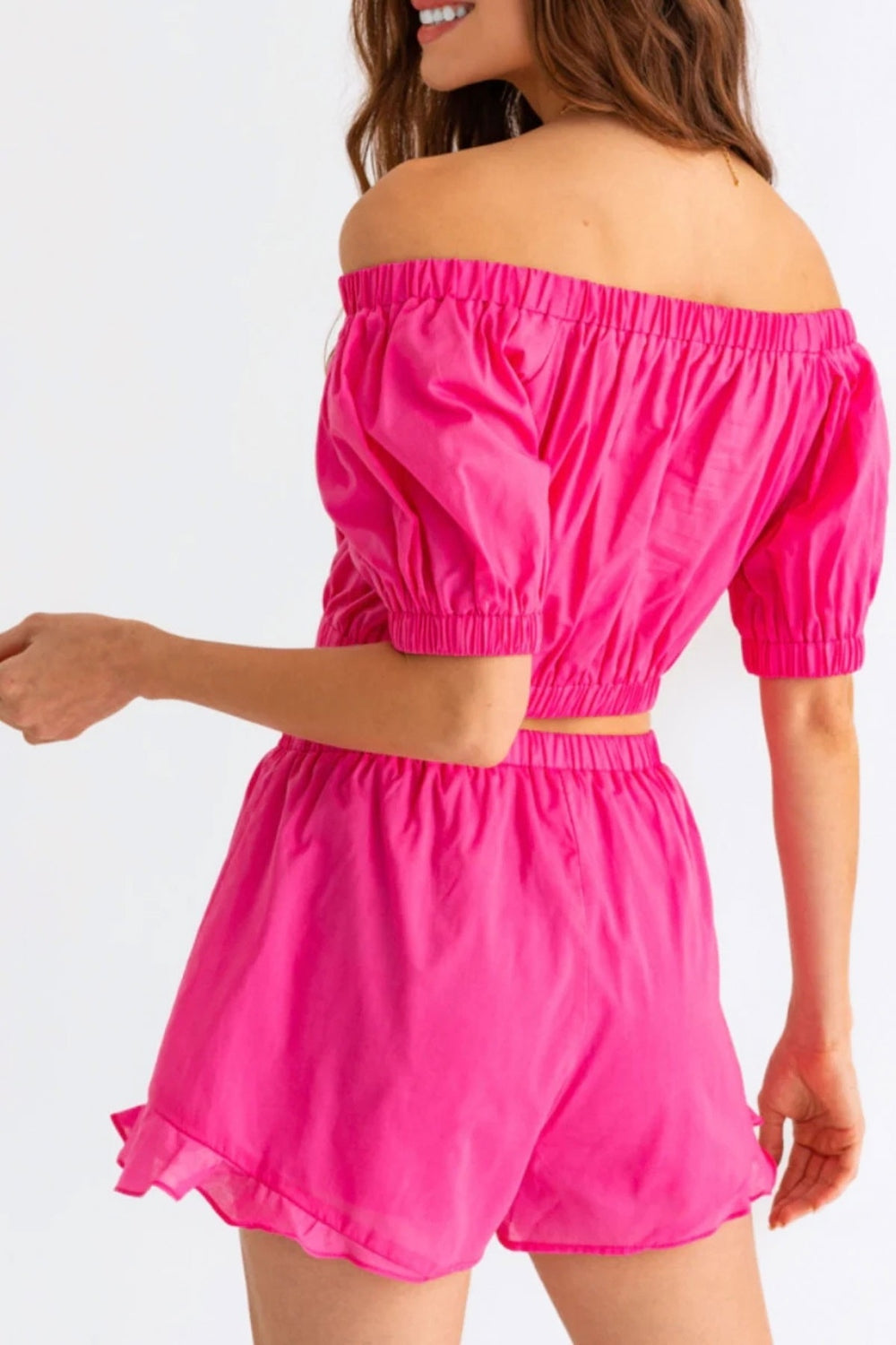 Person wearing the Le Lis Off Shoulder Crop Top and Ruffled Shorts Set, featuring a bright pink, off-the-shoulder crop top with puffed sleeves paired with matching high-waisted ruffled shorts, the perfect summer outfit.