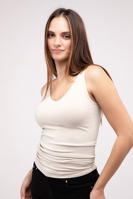 A woman in a white Front & Back 2-Way V-Neck Seamless Tank and black pants, standing with hands on hips and looking at the camera.