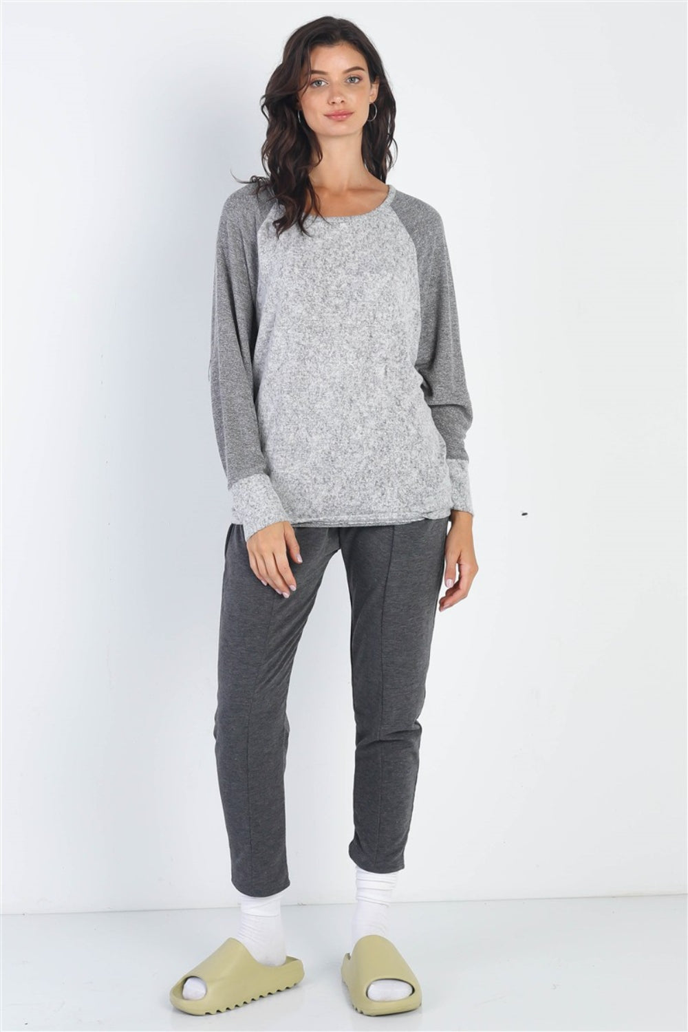 A woman stands wearing the Cherish Apparel Round Neck Long Sleeve Contrast Top in pink and gray with matching gray pants, set against a plain background.