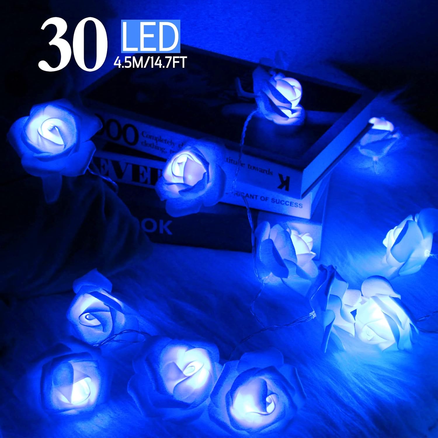 The Blue Rose Flower String Lights - 14.7ft 30 LED Fairy Lights Flower Garland Lights are elegantly draped over a stack of books and a framed photo, creating a romantic, glowing decor for any occasion, whether it's indoors or outdoors.