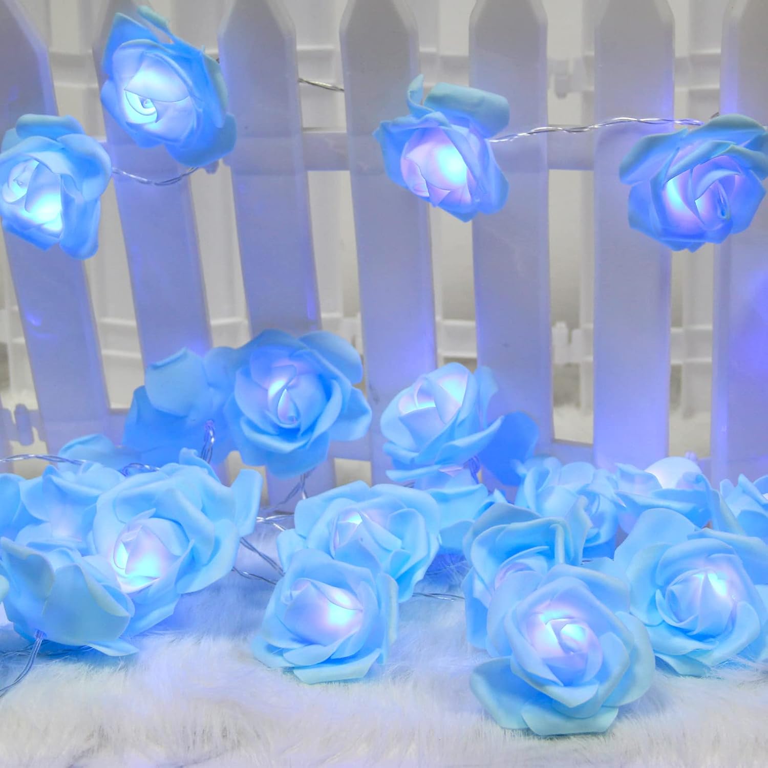 The Blue Rose Flower String Lights - 14.7ft 30 LED Fairy Lights Flower Garland Lights are elegantly draped over a stack of books and a framed photo, creating a romantic, glowing decor for any occasion, whether it's indoors or outdoors.