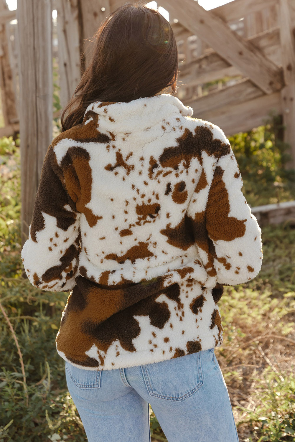 A person wearing a Zip Collar Cow Print Fleece Sweatshirt and light blue jeans stands outdoors with their back to the camera, showcasing the skin-friendly fleece material.