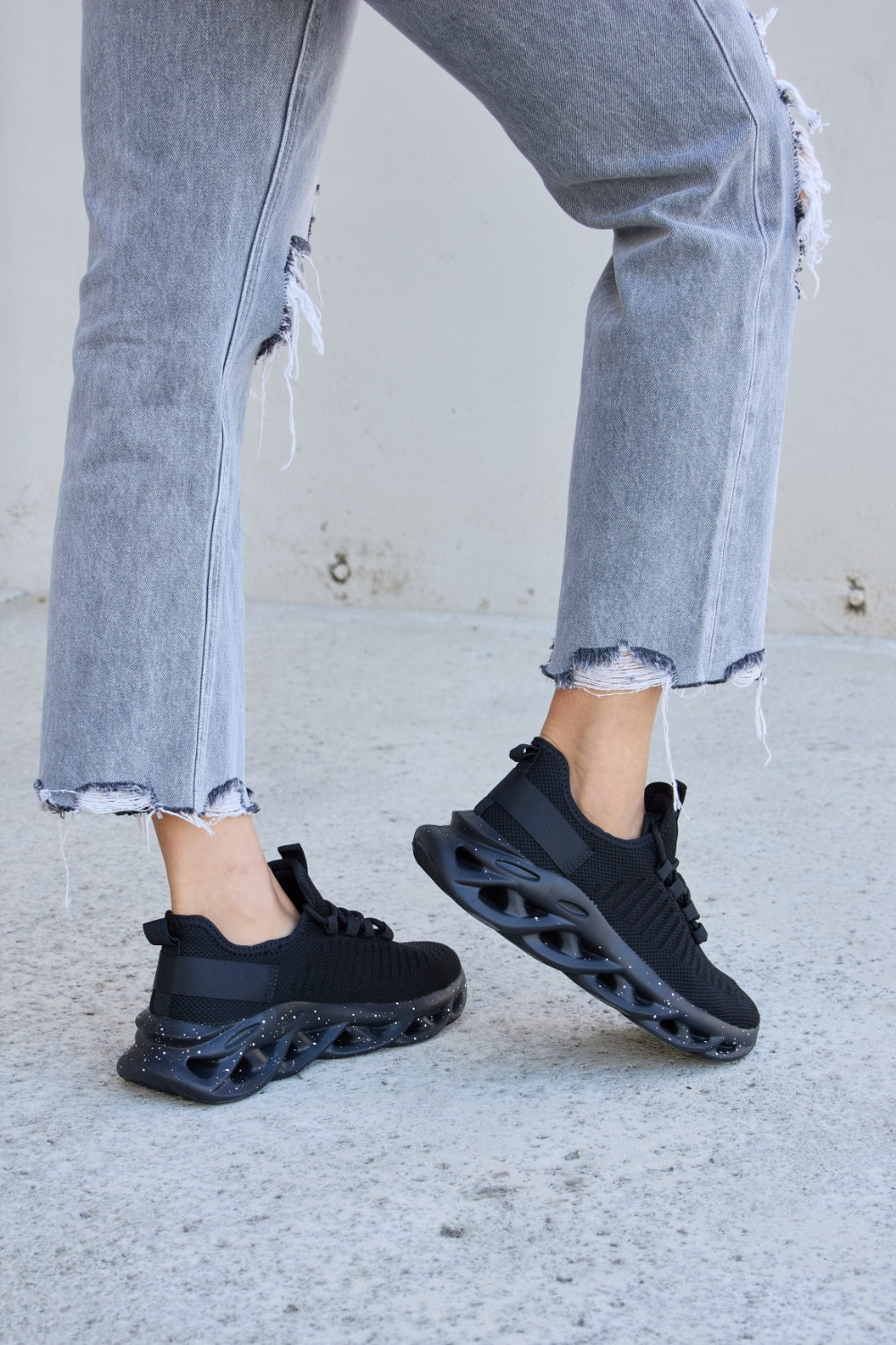 A person wearing ripped gray jeans and Forever Link Mesh Breathable Lace-Up Athletic Shoes is standing on a concrete surface.