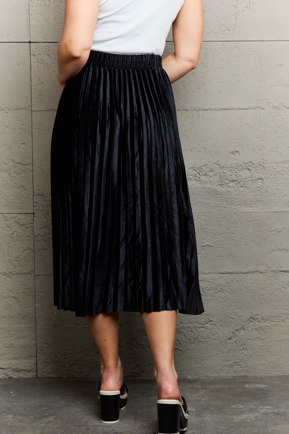 Person wearing a white sleeveless top, an elegant Ninexis Accordion Pleated Flowy Midi Skirt, and black platform sandals stands against a textured gray wall.