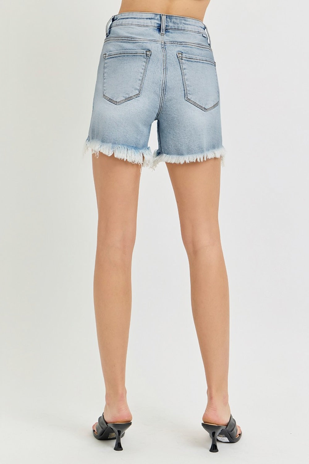 A person wearing the RISEN High Rise Side Step Hem Denim Shorts featuring light-wash, frayed hems, front pockets, and a versatile design.