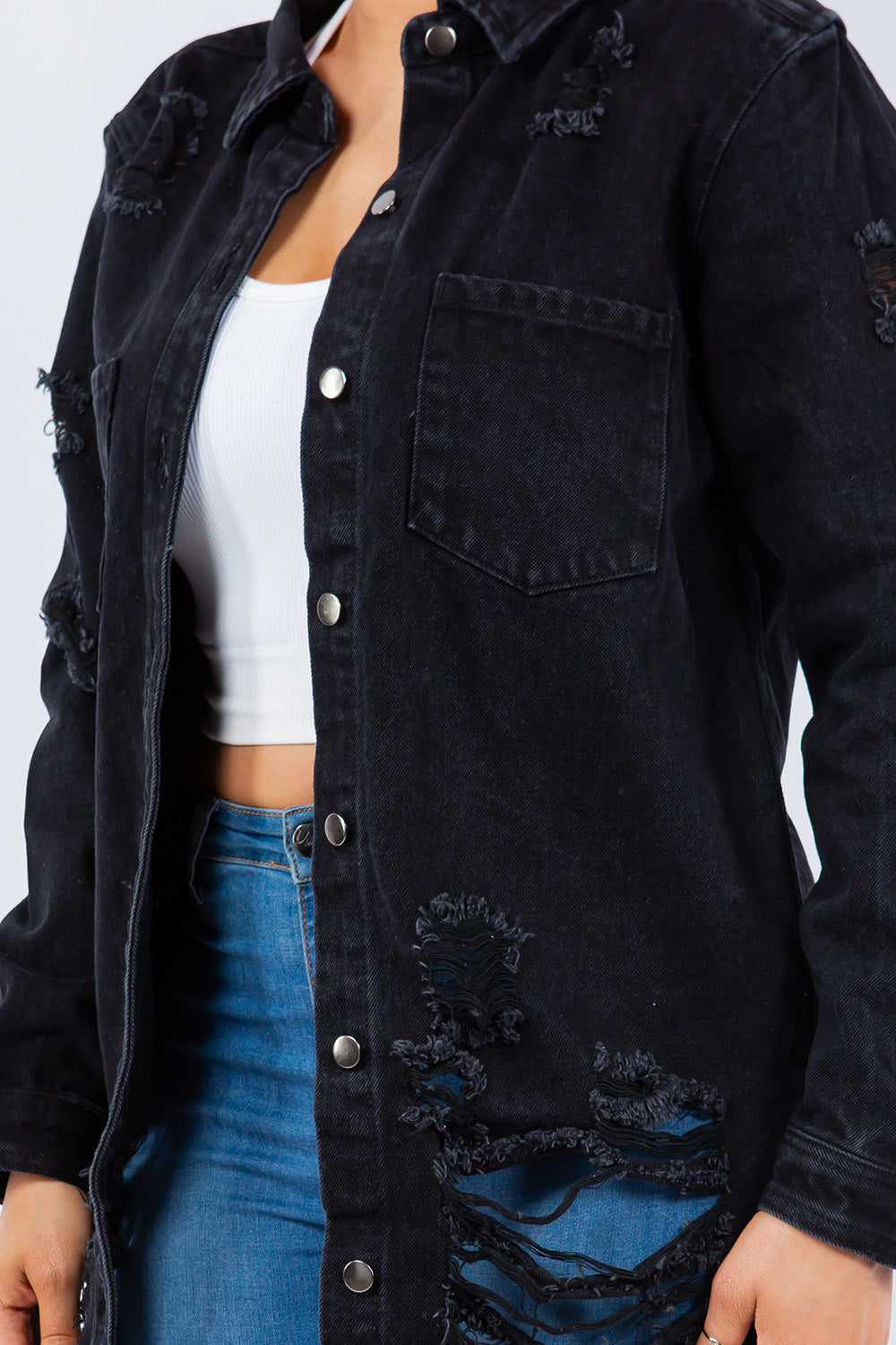 A person wearing an American Bazi Distressed Button Up Long Sleeve Denim Jacket over a white top and blue jeans stands against a plain background.