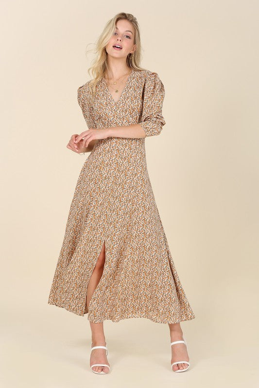 A woman gracefully poses against a beige background wearing the Fit and Flare floral maxi dress, featuring a V-neckline, elegant puff sleeves, and a complementary front slit.