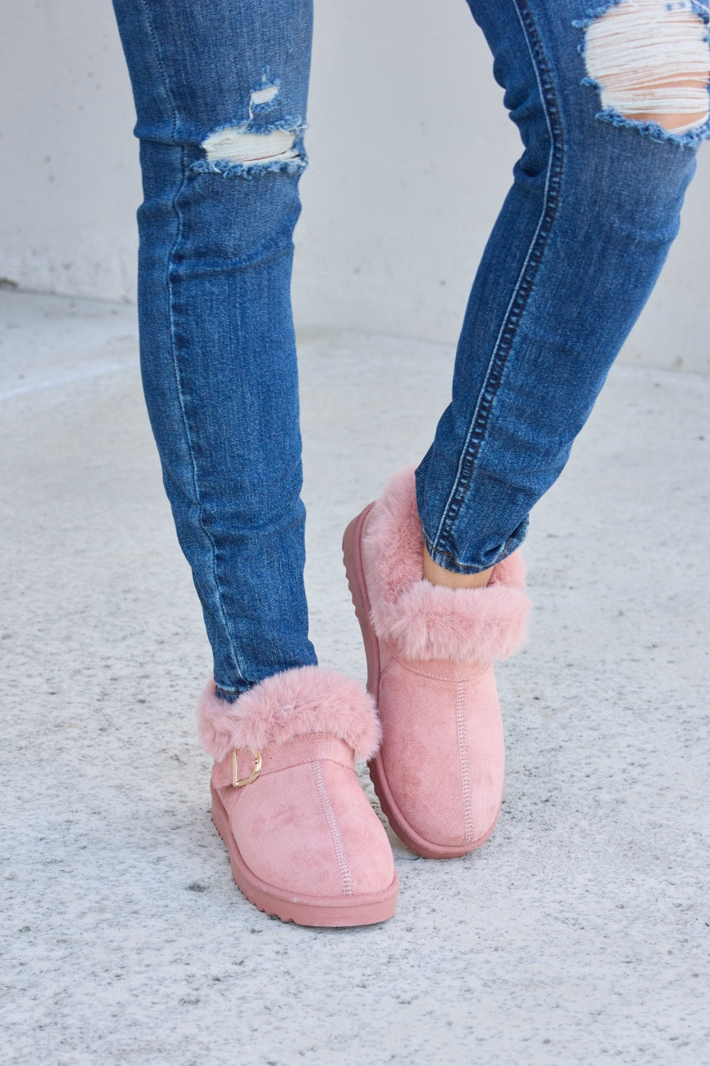 A person stands on a concrete surface, sporting ripped blue jeans and the Forever Link Furry Chunky Thermal Ankle Boots. The furry lining of these fashionable boots suggests both comfort and warmth for winter.