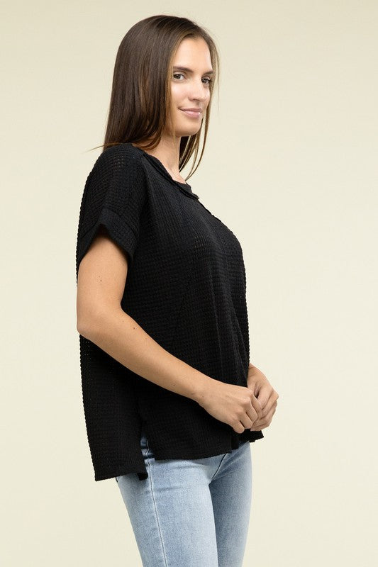 A woman with long brown hair is wearing a purple Brushed Waffle Exposed-Seam Short Sleeve Top and blue jeans, standing against a plain beige background. This casual wardrobe choice, with its short sleeves and side slits, is perfect for everyday wear.