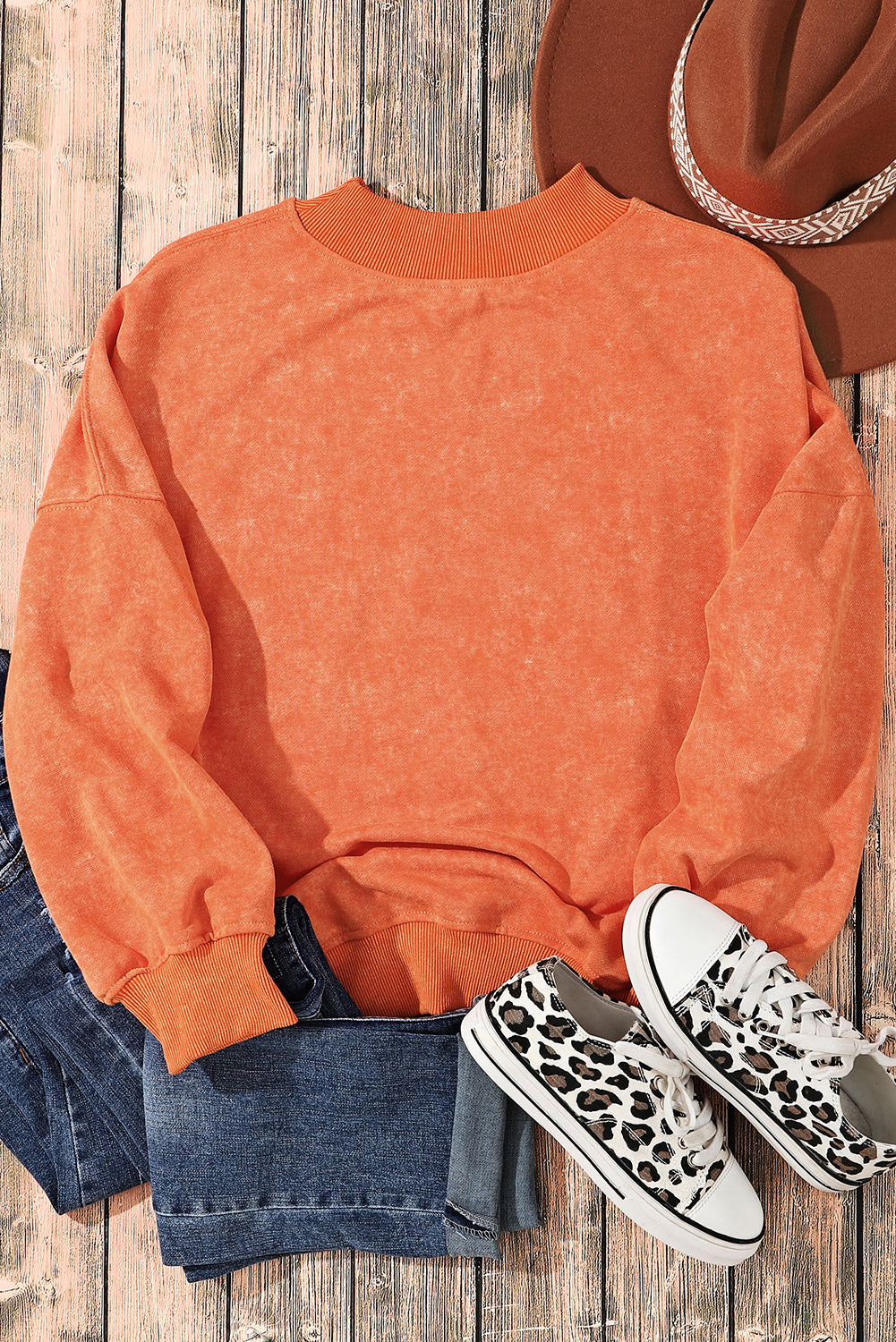 A person with long blonde hair wearing an Orange Drop Shoulder Crew Neck Pullover Sweatshirt and blue jeans stands with their back to the camera in a sunflower field.