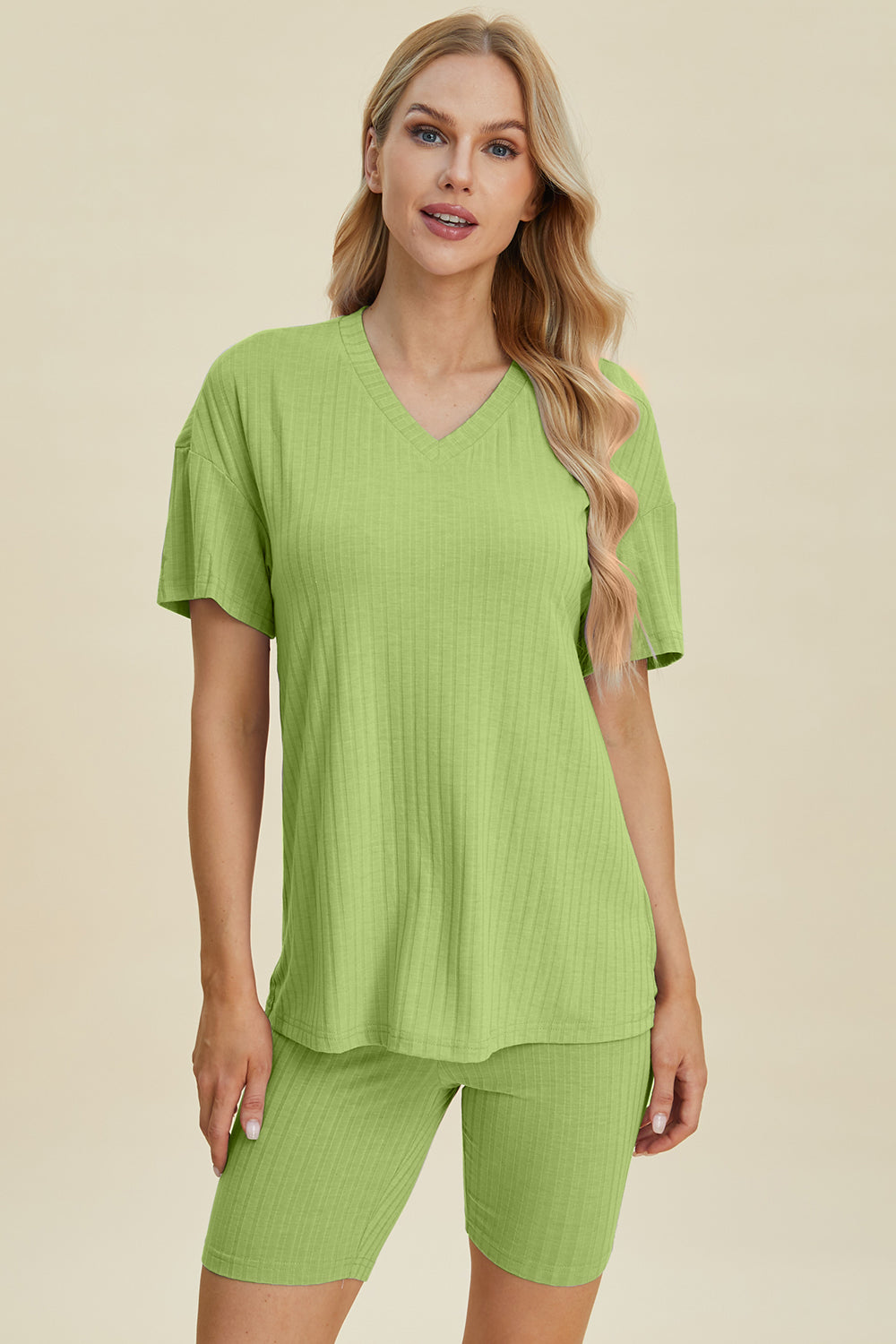 A woman with long blonde hair wearing the Basic Bae Full Size Ribbed V-Neck Short Sleeve Top and Shorts Set in rust stands against a plain background. This stylish two-piece set is made from a comfortable, stretchy fabric that is also machine washable.