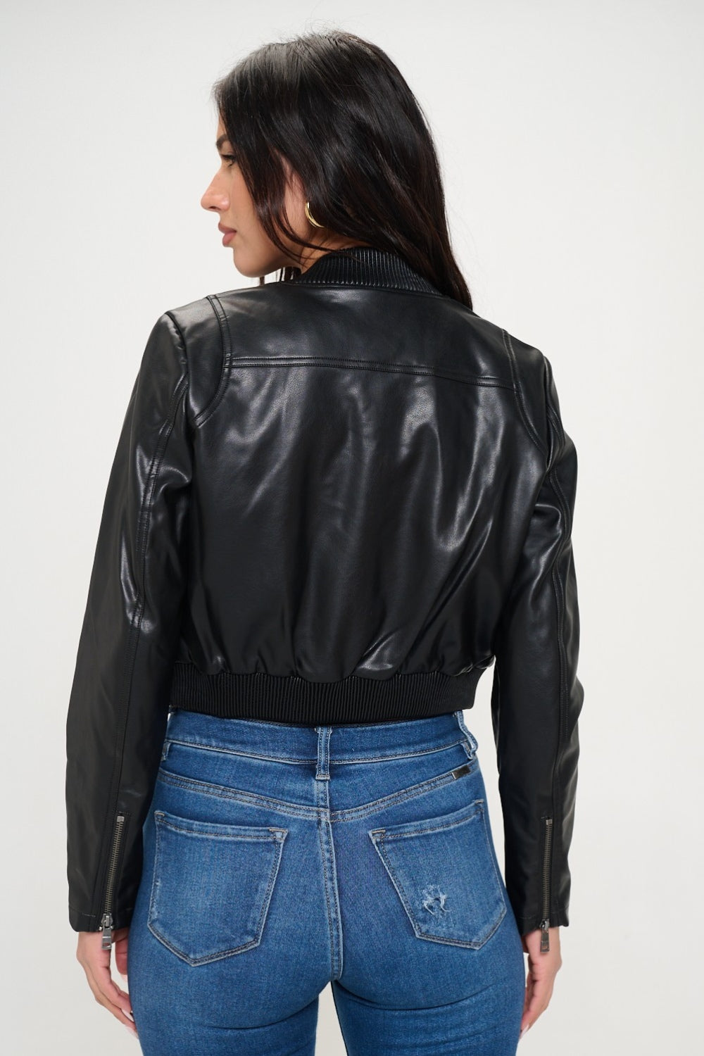 A woman wearing a Coalition LA Zip Up Cropped Bomber Jacket over a black crop top and blue jeans with buttons, looking at the camera with her hands in her jacket pockets.