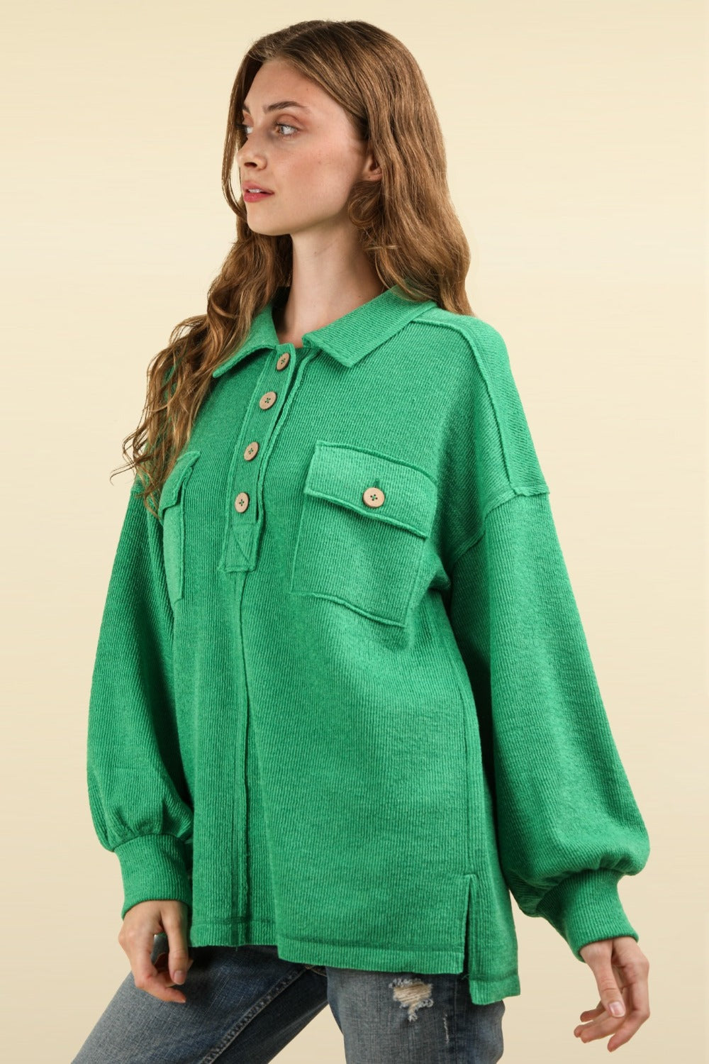 A person with long hair wearing an oversized fit, green VERY J Collared Half Button Knit Top with Pockets stands against a beige background.