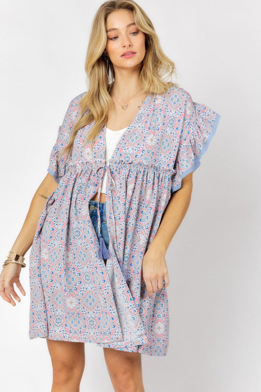 A woman stands against a white background wearing the Printed Short Sleeve Ruffle Kimono over a white top and denim shorts, effortlessly blending style and comfort.