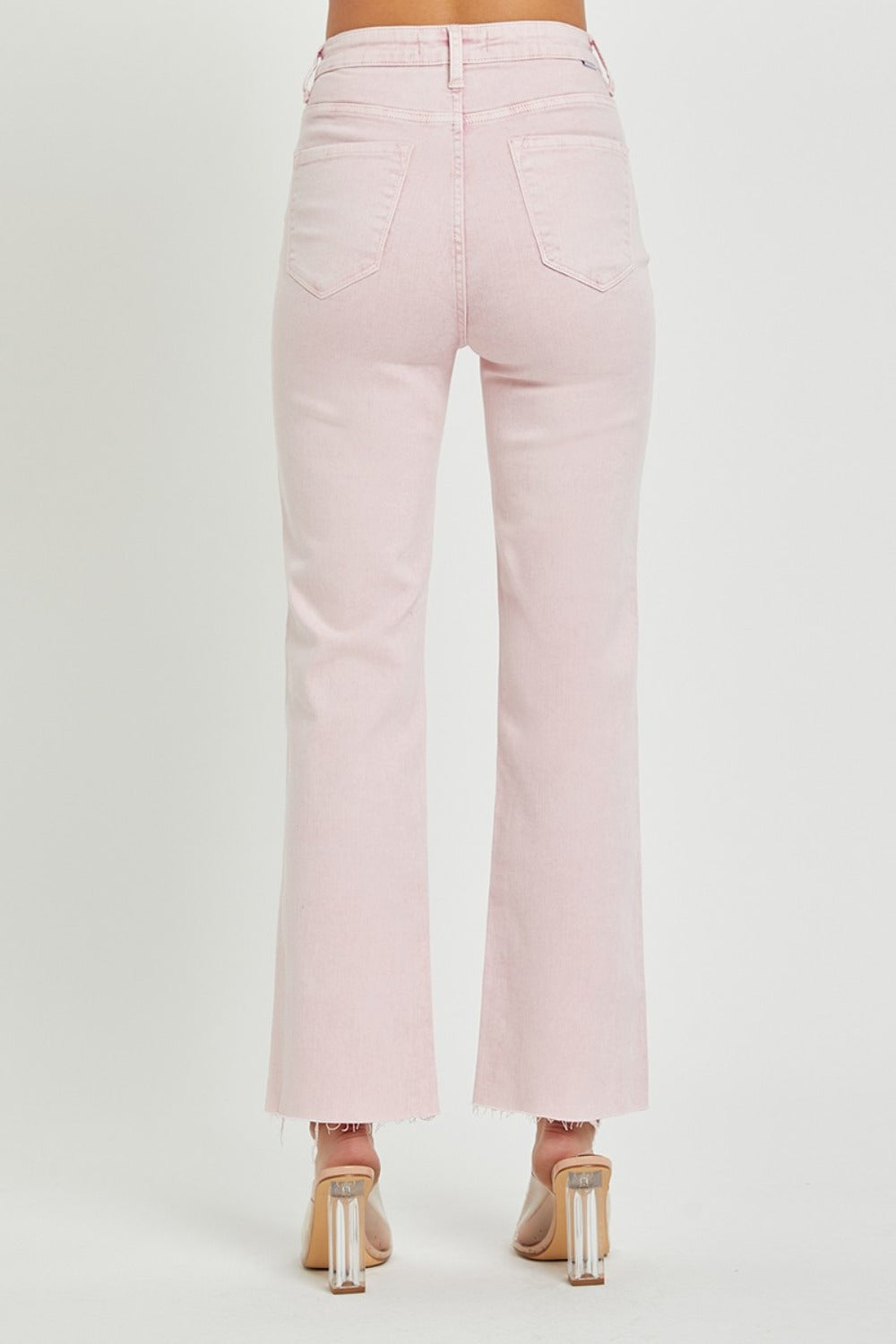 Person wearing RISEN Full Size High Rise Tummy Control Straight Jeans in light pink with a raw hem and clear heeled shoes against a plain white background.