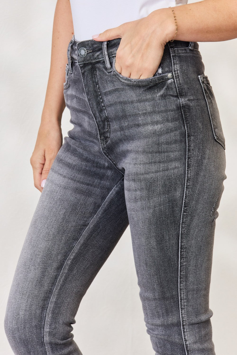 A person wearing the Judy Blue Full Size High Waist Tummy Control Release Hem Skinny Jeans paired with nude heels stands against a light background.