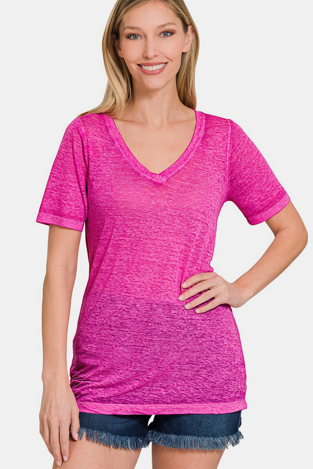 A woman is smiling and standing with her hand on her hip, wearing a pink Zenana V-Neck Short Sleeve T-Shirt made from comfortable fabric paired with denim shorts.