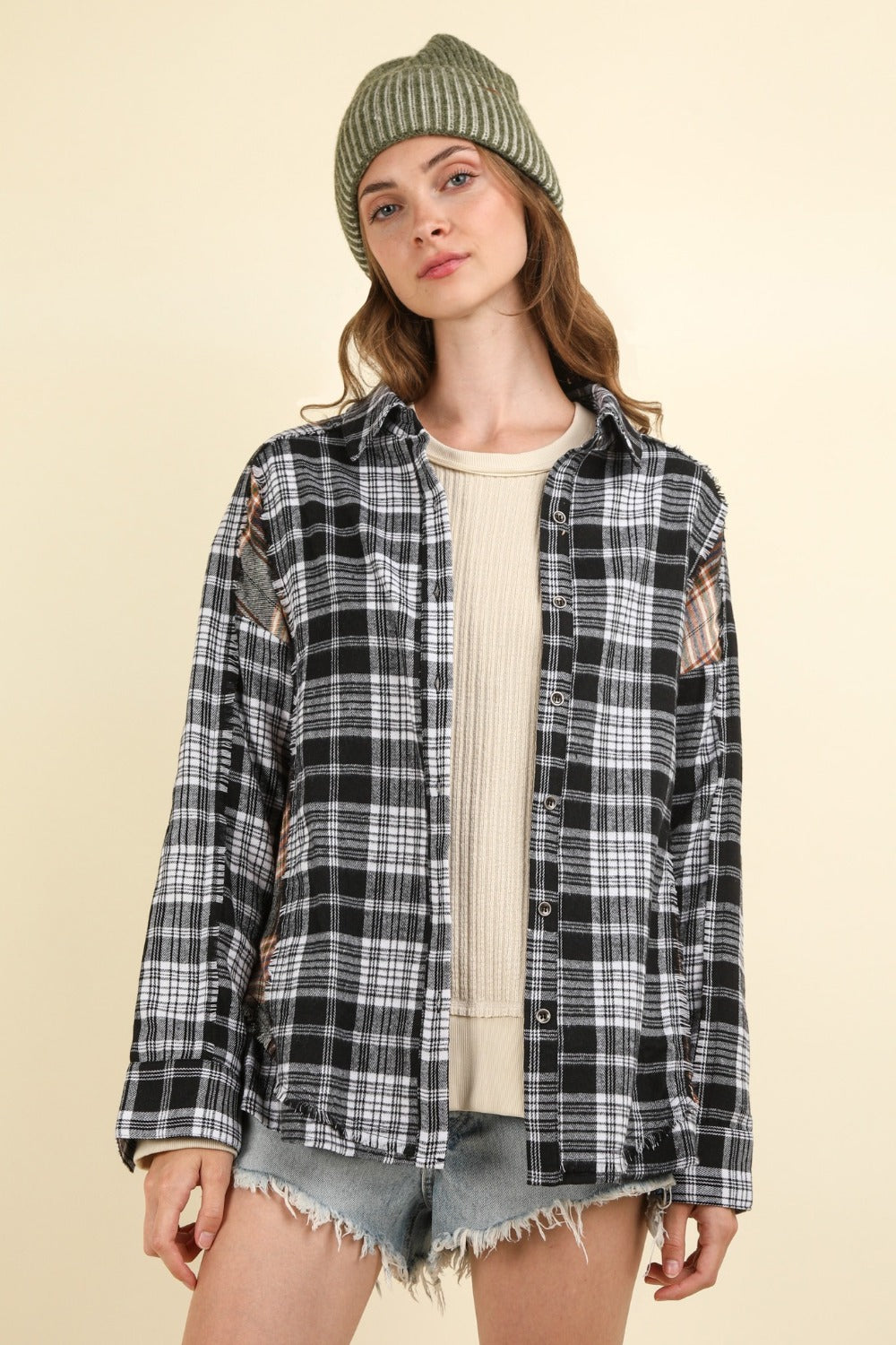 A person wearing an oversized VERY J Contrast Plaid Raw Detail Shirt, a beige beanie, and denim shorts stands against a plain background.