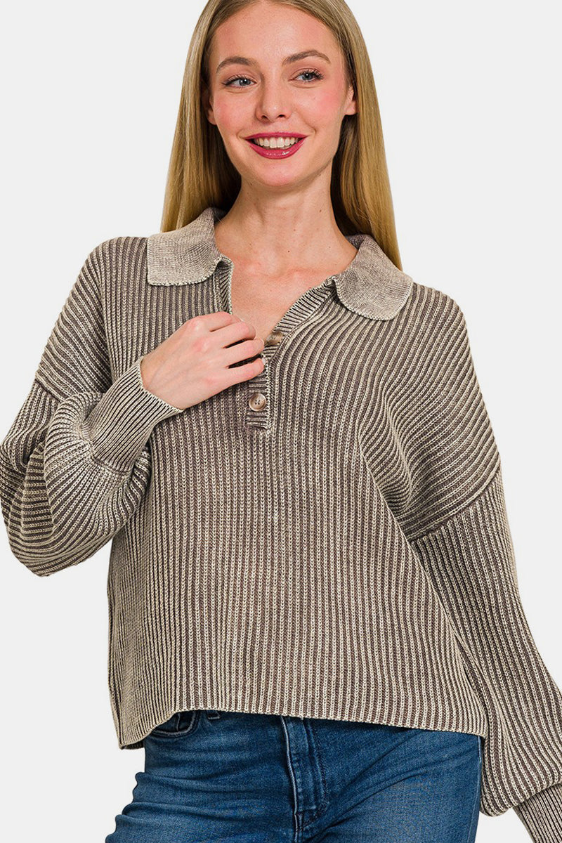 A woman with long blonde hair wearing the Zenana Washed Half Button Long Sleeve Sweater, made of 100% cotton and featuring a striped oversized design, pairs it with jeans as she stands against a plain background, smiling with one hand touching the sweater's collar.